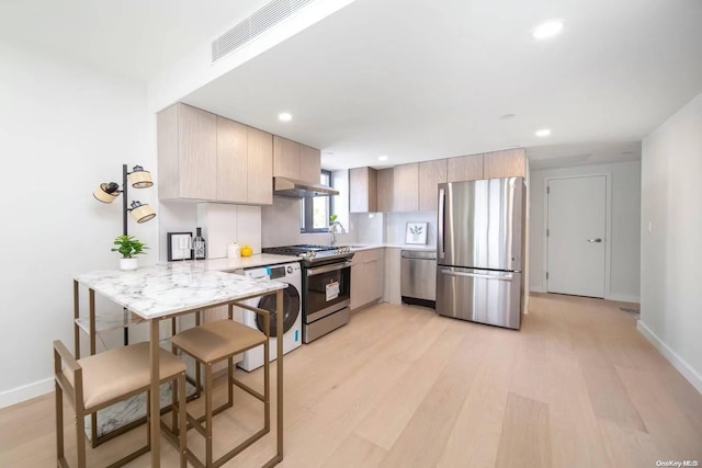 kitchen with stainless steel appliances, light hardwood / wood-style flooring, kitchen peninsula, light brown cabinetry, and exhaust hood