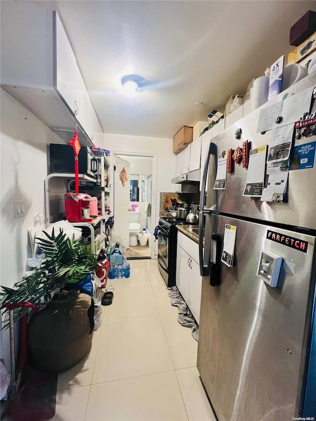 kitchen with light tile patterned flooring, black stove, white cabinetry, and stainless steel refrigerator