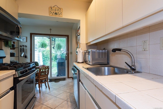 kitchen featuring stainless steel appliances, sink, light tile patterned floors, tile countertops, and white cabinetry