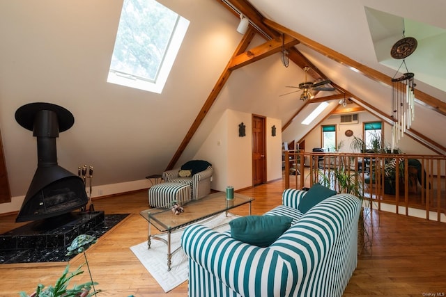 living room featuring hardwood / wood-style floors, a skylight, a wood stove, and ceiling fan