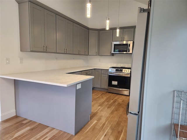 kitchen with kitchen peninsula, appliances with stainless steel finishes, light hardwood / wood-style floors, and pendant lighting