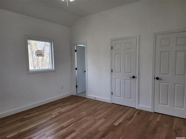 unfurnished bedroom with two closets, dark hardwood / wood-style flooring, and lofted ceiling