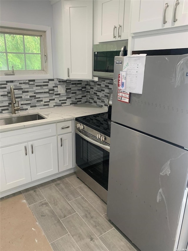 kitchen featuring white cabinetry, sink, light stone counters, light hardwood / wood-style flooring, and appliances with stainless steel finishes