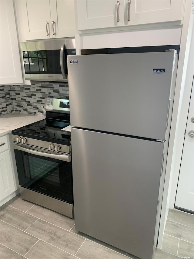 kitchen with decorative backsplash, light stone counters, white cabinets, and appliances with stainless steel finishes