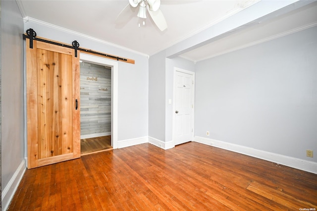 unfurnished bedroom with hardwood / wood-style flooring, ceiling fan, a barn door, ornamental molding, and a closet