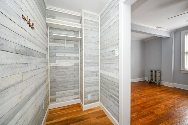 hallway with hardwood / wood-style flooring, crown molding, radiator, and wooden walls