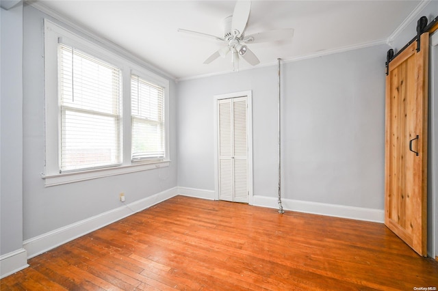 unfurnished bedroom with a barn door, ceiling fan, hardwood / wood-style floors, and crown molding