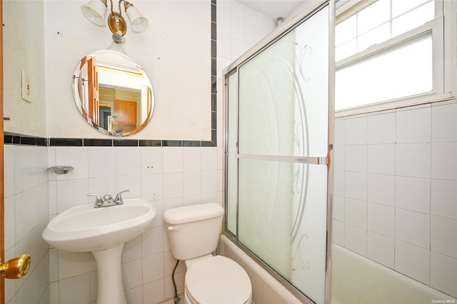 bathroom with shower / bath combination with glass door, toilet, and tile walls