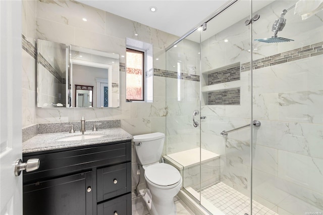 bathroom featuring vanity, toilet, a shower with shower door, and tile walls