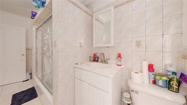 full bathroom with vanity, bath / shower combo with glass door, tile patterned flooring, toilet, and tile walls