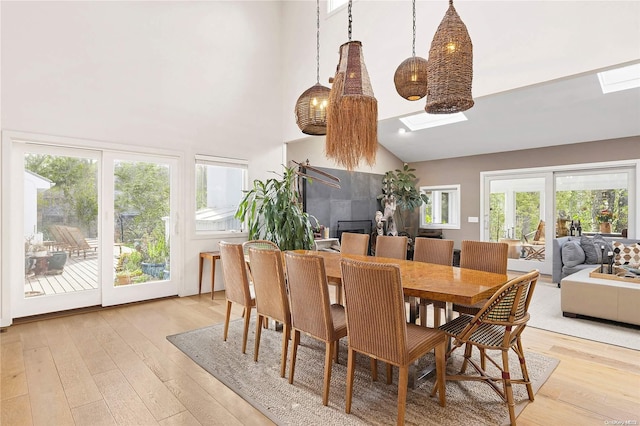 dining area featuring light wood-type flooring, a skylight, and high vaulted ceiling