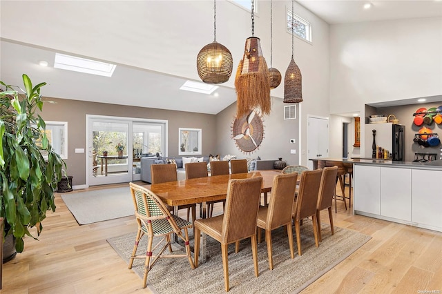 dining room featuring a skylight, high vaulted ceiling, and light wood-type flooring