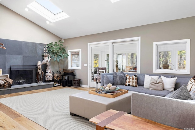 living room with a tile fireplace, vaulted ceiling with skylight, and hardwood / wood-style floors