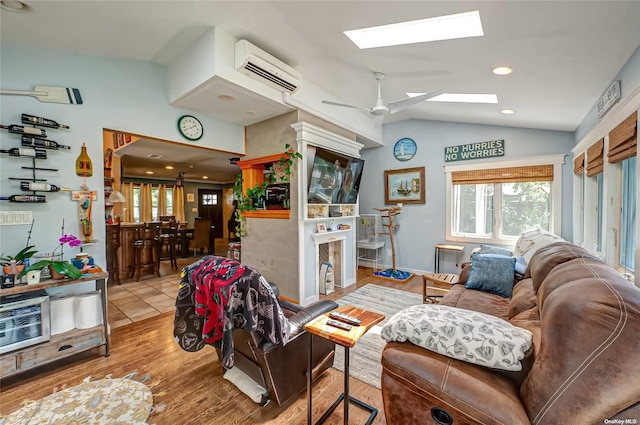 living room featuring a wall unit AC, ceiling fan, vaulted ceiling with skylight, and light hardwood / wood-style floors