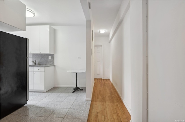 kitchen featuring white cabinets, black fridge, sink, light hardwood / wood-style flooring, and tasteful backsplash