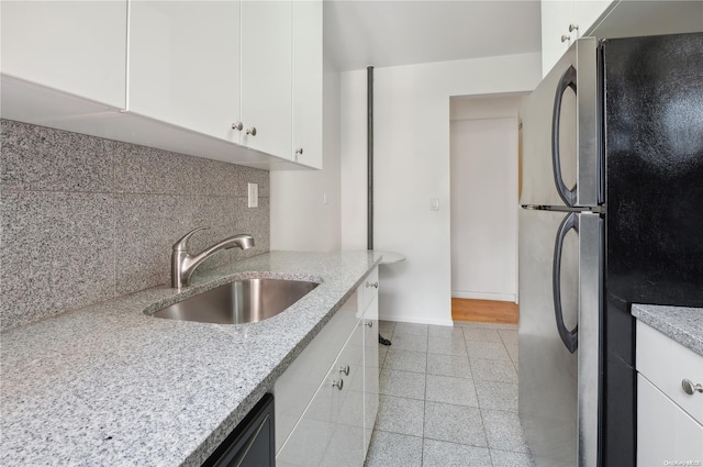 kitchen with tasteful backsplash, light stone counters, black fridge, sink, and white cabinetry