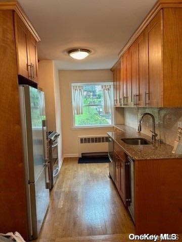 kitchen with refrigerator, radiator, sink, light hardwood / wood-style flooring, and stainless steel range with gas cooktop