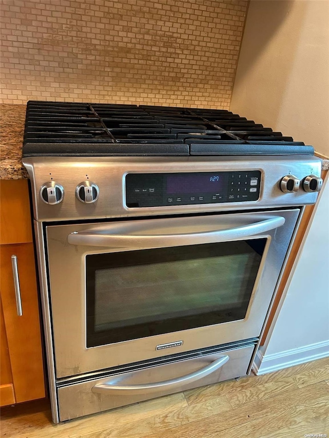 details with dark stone counters, backsplash, light hardwood / wood-style floors, and high end stainless steel range oven