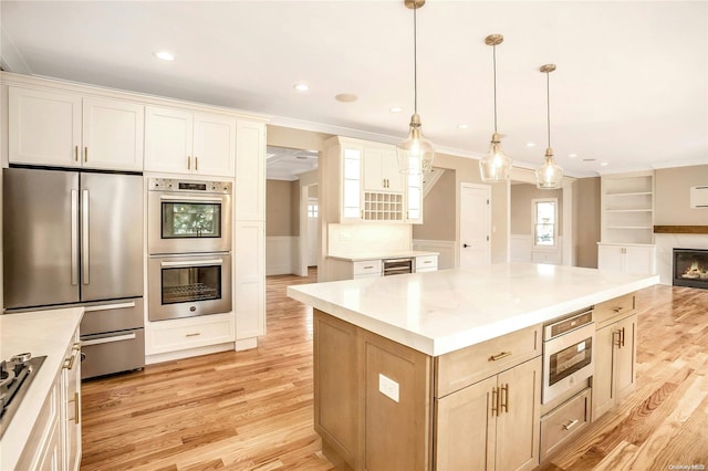 kitchen with a center island, hanging light fixtures, stainless steel appliances, crown molding, and light wood-type flooring