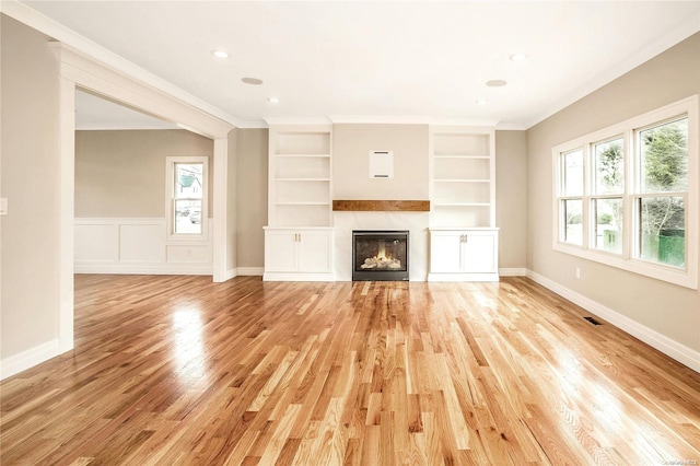 unfurnished living room featuring built in shelves, crown molding, and light wood-type flooring