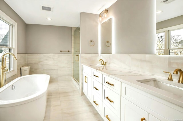 bathroom featuring plus walk in shower, vanity, a healthy amount of sunlight, and tile walls