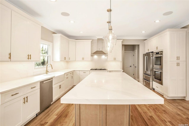 kitchen featuring a center island, light hardwood / wood-style flooring, wall chimney exhaust hood, decorative light fixtures, and stainless steel appliances