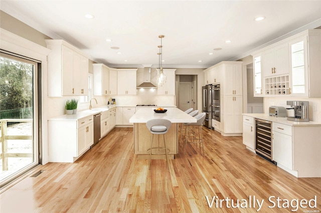 kitchen with a kitchen island, beverage cooler, wall chimney range hood, and light wood-type flooring