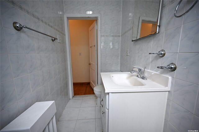 bathroom with toilet, vanity, tile patterned floors, and tile walls