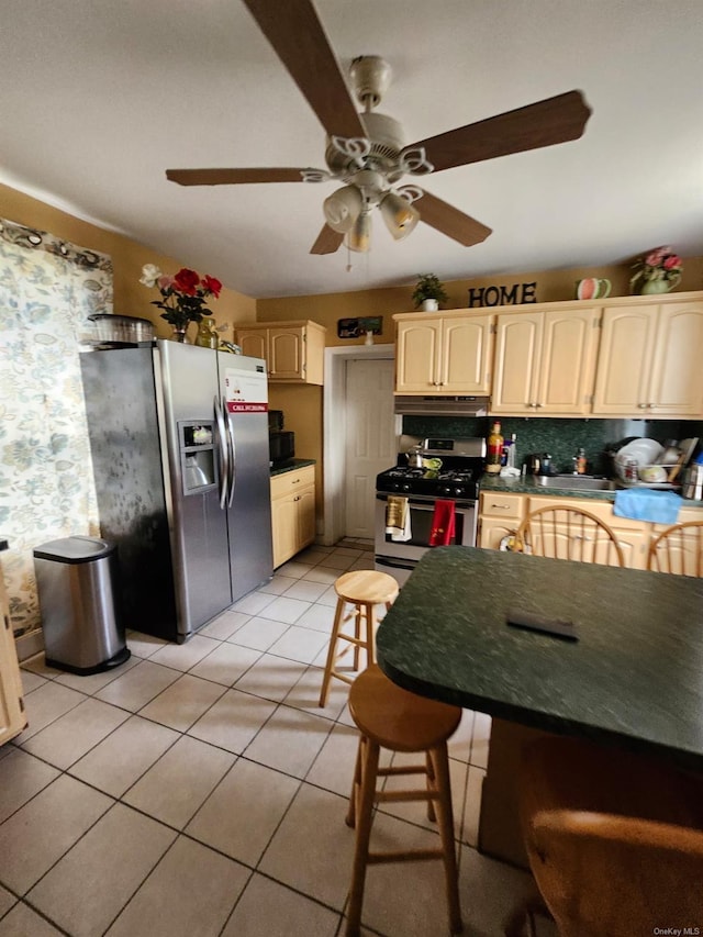 kitchen with appliances with stainless steel finishes, light tile patterned floors, ceiling fan, and a kitchen breakfast bar