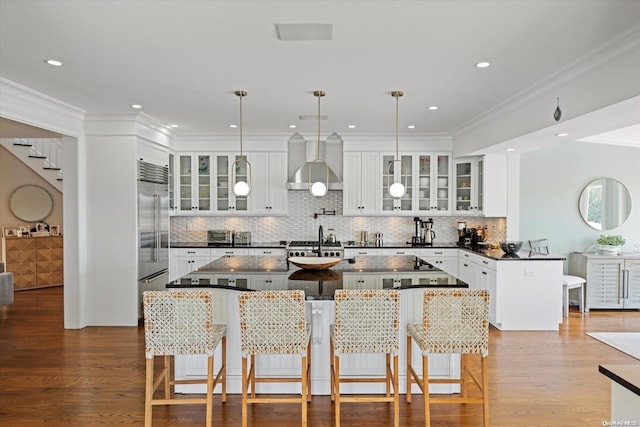 kitchen with wall chimney range hood, a kitchen breakfast bar, decorative light fixtures, white cabinets, and hardwood / wood-style flooring