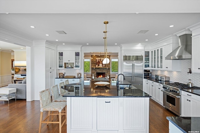 kitchen featuring wall chimney exhaust hood, dark hardwood / wood-style flooring, a large island with sink, pendant lighting, and high quality appliances