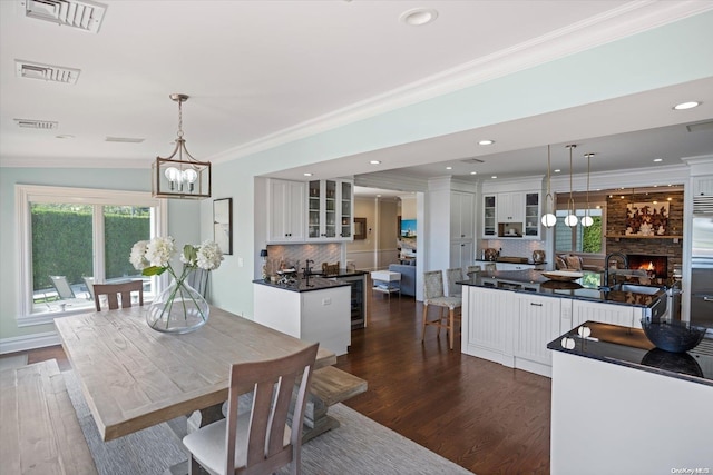 dining space with dark wood-type flooring, a stone fireplace, sink, ornamental molding, and a chandelier