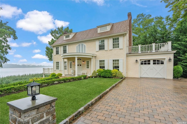 view of front of home featuring a front yard, a balcony, a garage, a water view, and a porch