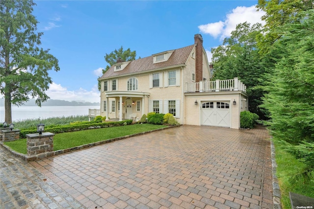 view of front facade featuring a front yard, a water view, a garage, and a balcony