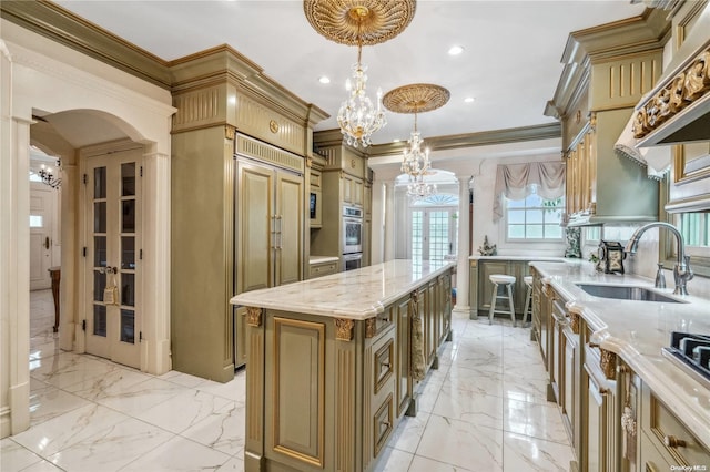 kitchen with light stone countertops, crown molding, sink, a kitchen island, and hanging light fixtures