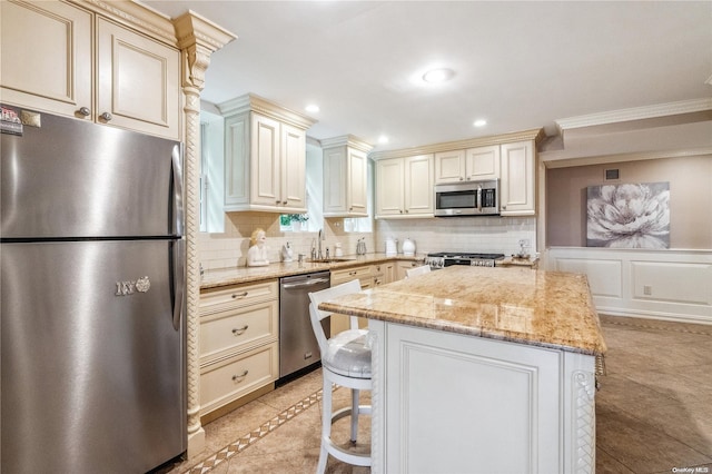 kitchen featuring sink, light stone counters, cream cabinets, a breakfast bar area, and appliances with stainless steel finishes