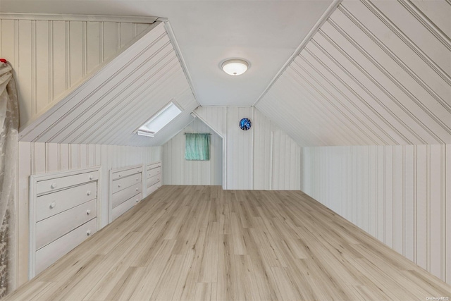 additional living space with wooden walls, vaulted ceiling with skylight, and light hardwood / wood-style floors