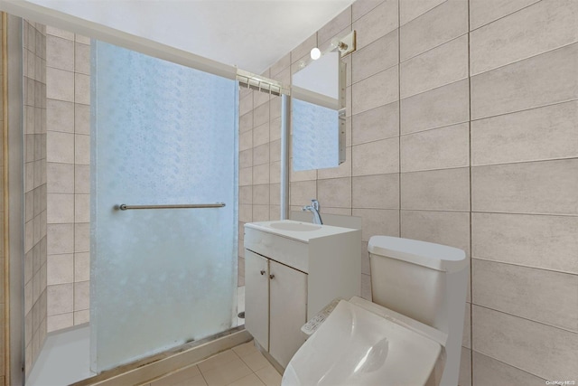 bathroom with tile patterned flooring, toilet, vanity, a shower with shower door, and tile walls