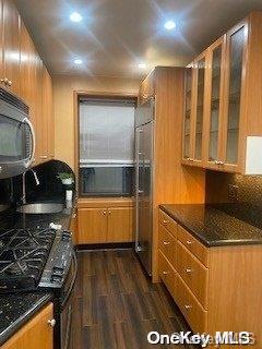 kitchen featuring sink, black range oven, dark wood-type flooring, cooling unit, and dark stone counters