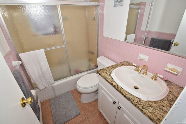 full bathroom featuring vanity, combined bath / shower with glass door, tile patterned flooring, toilet, and tile walls