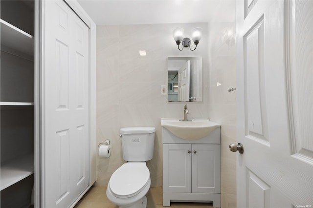 bathroom featuring tile patterned flooring, vanity, toilet, and tile walls