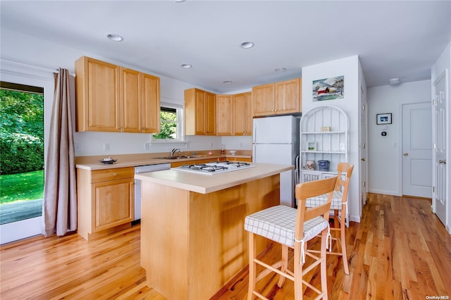 kitchen with a kitchen bar, a kitchen island, white appliances, and light hardwood / wood-style floors