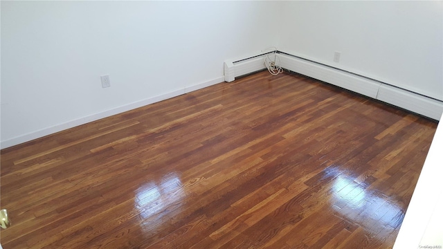 spare room featuring baseboard heating and dark hardwood / wood-style floors