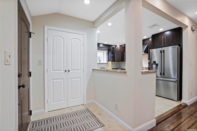 kitchen featuring lofted ceiling, light wood-type flooring, high quality fridge, tasteful backsplash, and dark brown cabinets