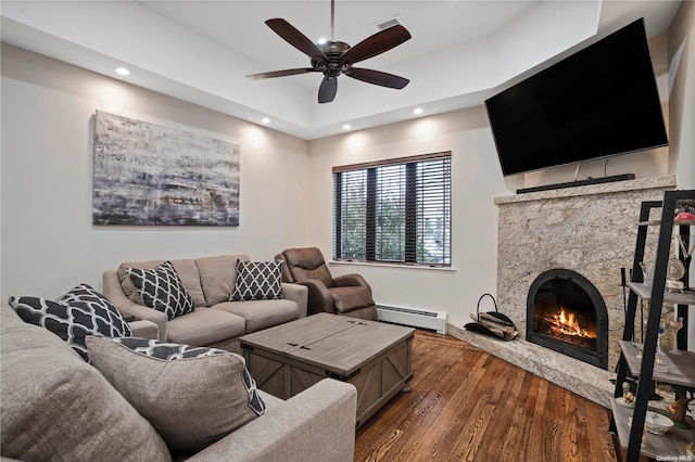 living room with a high end fireplace, a baseboard heating unit, ceiling fan, and dark wood-type flooring