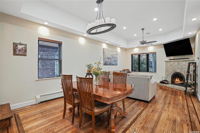 dining area featuring a raised ceiling, a fireplace, hardwood / wood-style floors, and a baseboard radiator