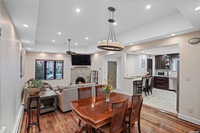 dining space with hardwood / wood-style floors, a baseboard heating unit, a raised ceiling, ceiling fan, and a fireplace