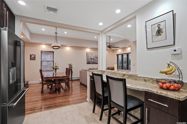 kitchen featuring high quality fridge, a breakfast bar, dark brown cabinets, ceiling fan, and light hardwood / wood-style flooring