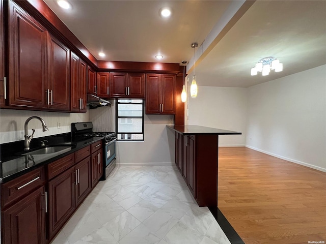 kitchen with kitchen peninsula, light wood-type flooring, sink, pendant lighting, and black gas stove