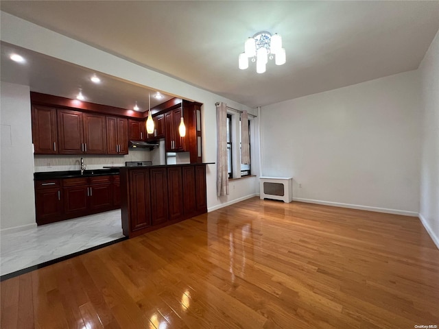 kitchen featuring light wood-type flooring, backsplash, sink, pendant lighting, and an inviting chandelier